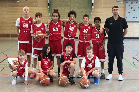Basketballmannschaft der RheinStars Köln posiert mit Trainer in der Sporthalle.