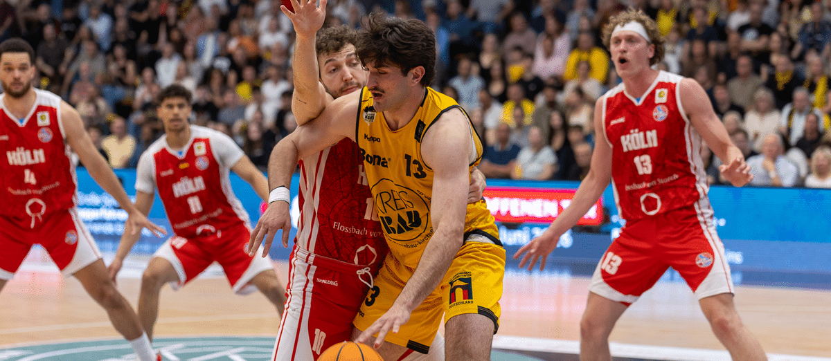 Basketballspiel der RheinStars Köln gegen Team in Gelb, Spieler mit Ball umgeben von Gegnern in Rot.