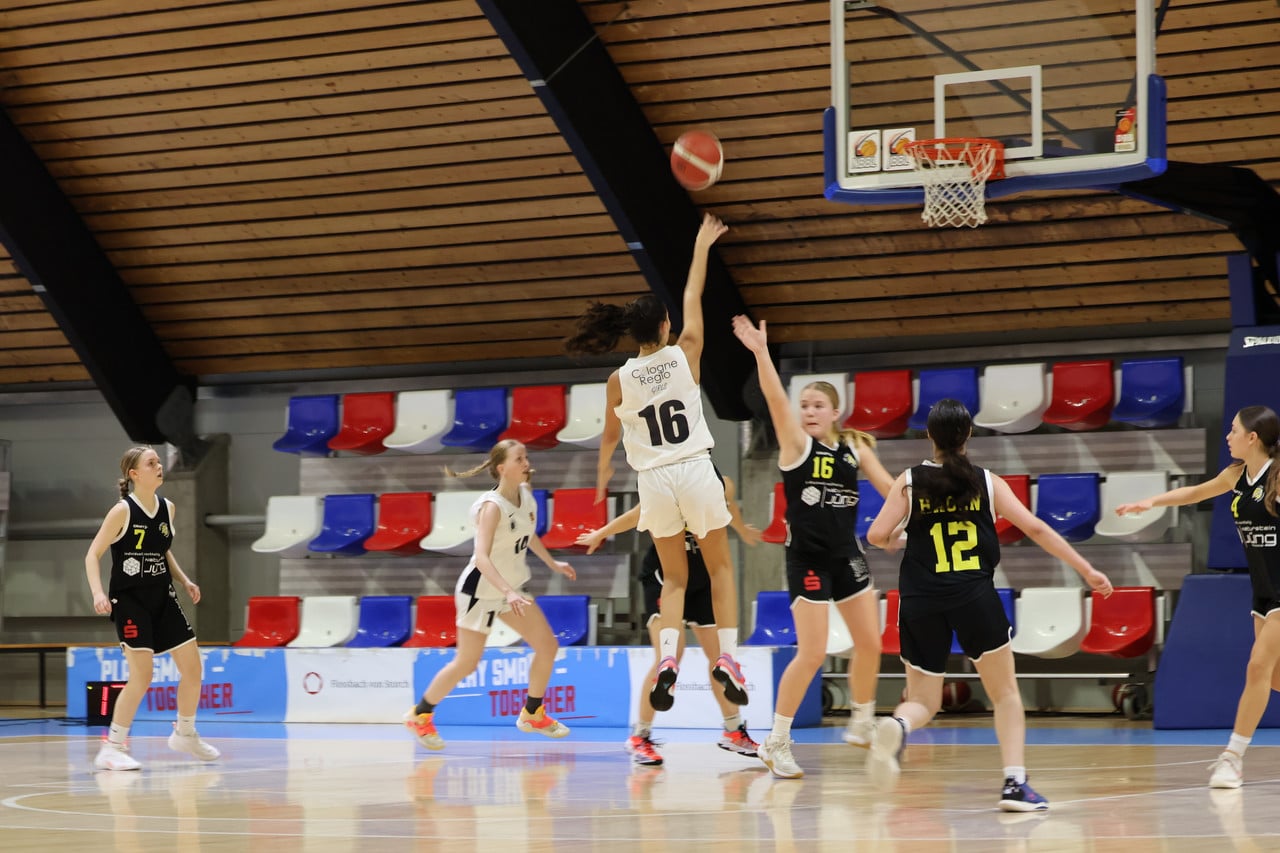 Basketballspiel der RheinStars Köln: Spielerin Nummer 16 wirft Ball auf Korb, Gegnerinnen verteidigen in schwarzen Trikots.