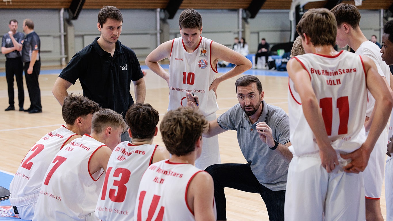 Trainer der RheinStars Köln gibt Anweisungen an seine Basketballmannschaft während einer Spielzeitpause in der Sporthalle.