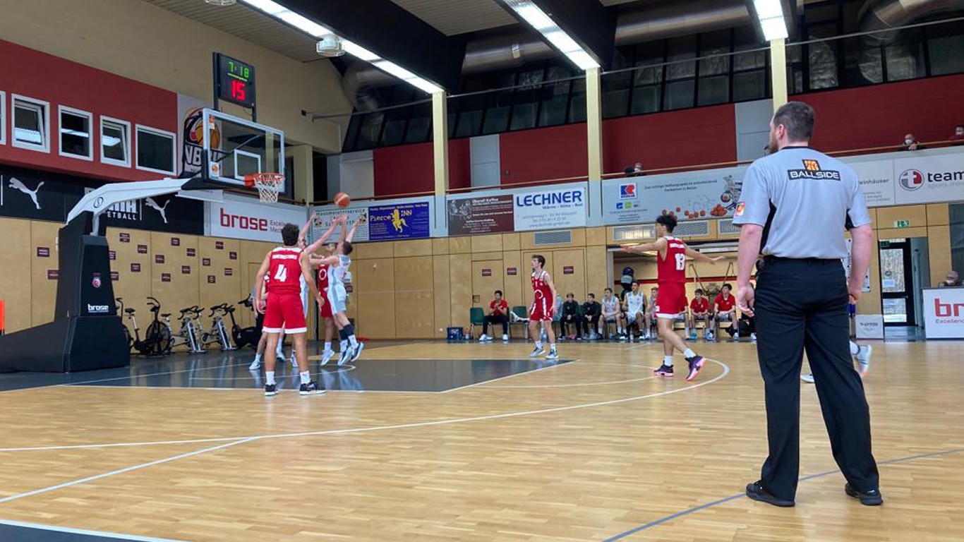 Basketballspiel der RheinStars Köln in einer Sporthalle mit roten und weißen Teams sowie Schiedsrichter.