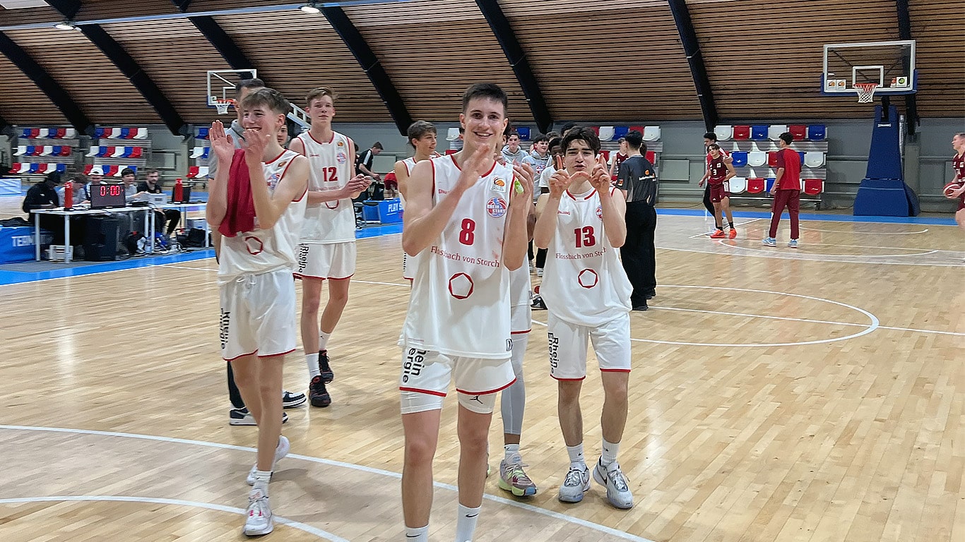 Basketballspieler der RheinStars Köln in weißen Trikots winken nach einem Spiel in einer Sporthalle.