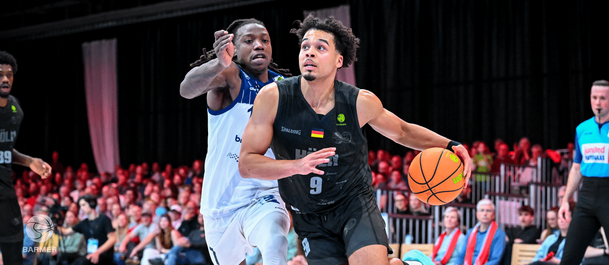 Basketballspiel der RheinStars Köln: Spieler in schwarzem Trikot dribbelt gegen Gegner in hellblauem Trikot.