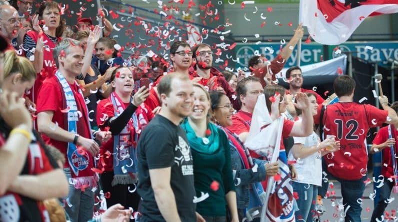 Fans der RheinStars Köln feiern mit roten und weißen Konfetti beim Sieg.