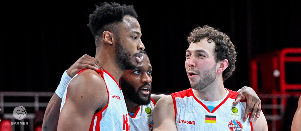Drei Basketballspieler der RheinStars Köln in weißen Trikots stehen zusammen.