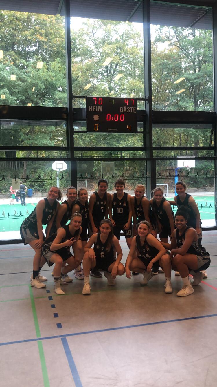 Basketballmannschaft RheinStars Köln posiert in schwarzen Trikots in einer Sporthalle.