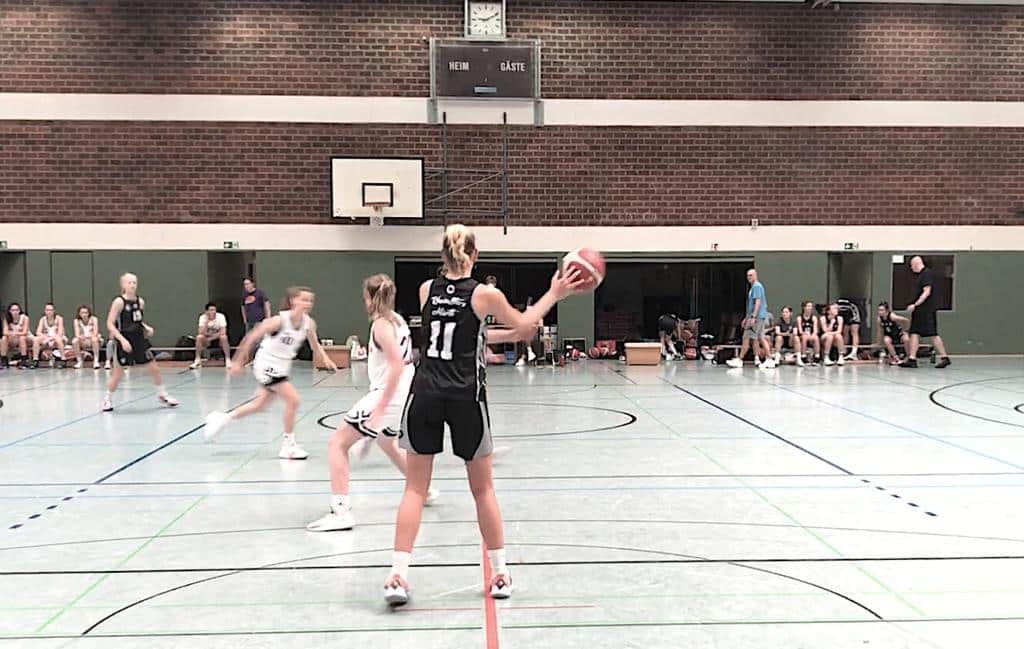 Basketballspiel der RheinStars Köln in einer Sporthalle; Spielerin in schwarzem Trikot wirft Ball.