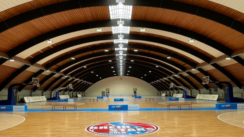 Sporthalle der RheinStars Köln mit Basketballplatz und gewölbter Holzdecke.