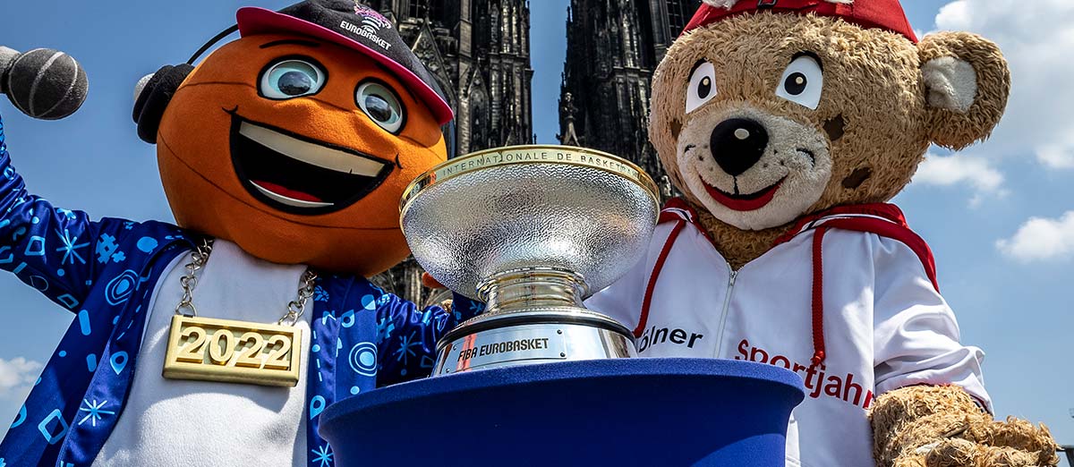 Zwei Maskottchen der RheinStars Köln präsentieren den EuroBasket-Pokal 2022 vor dem Kölner Dom.