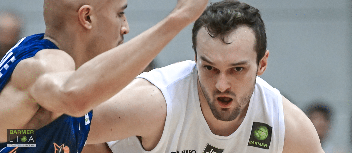 Basketballspieler der RheinStars Köln im weißen Trikot dribbelt gegen Gegner im blauen Trikot.