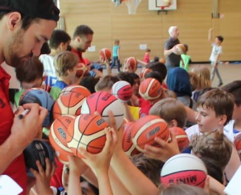 Spieler der RheinStars Köln signiert Basketbälle einer Gruppe von Kindern.