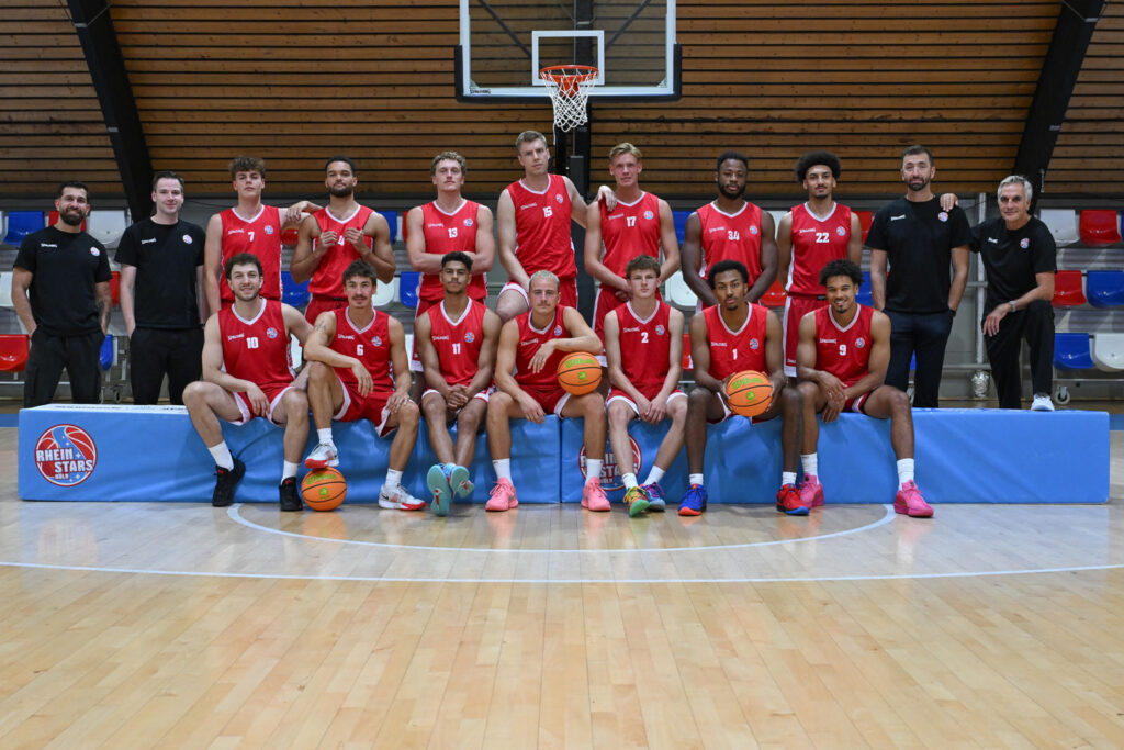 Mannschaftsfoto der RheinStars Köln Basketballmannschaft in der Sporthalle mit Trainerstab.