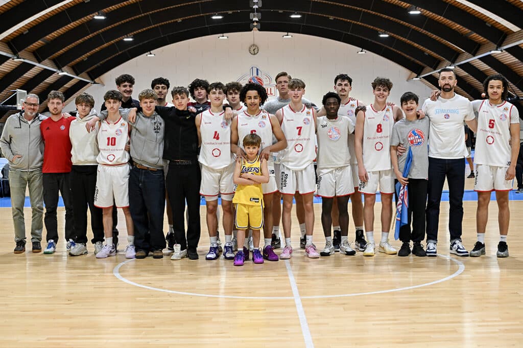 Jugend-Basketballmannschaft und Betreuer der RheinStars posieren gemeinsam in einer Sporthalle zum Teamfoto.