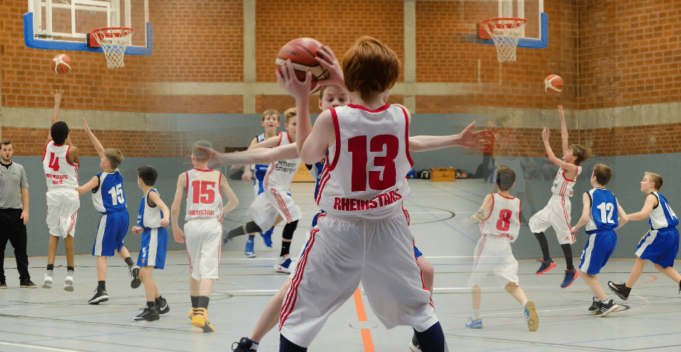 Kind der RheinStars Köln wirft Basketball mit ausgebreiteten Armen in Sporthalle.