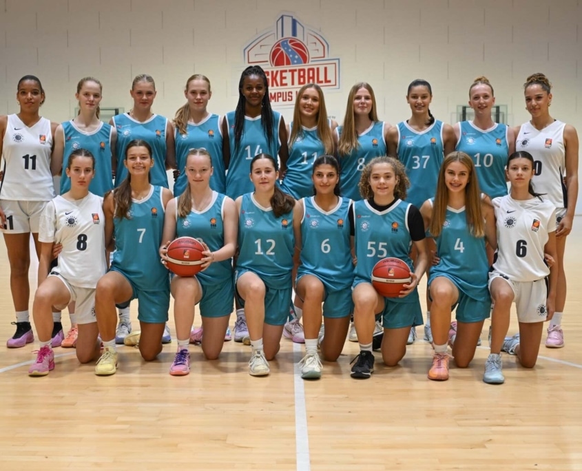 Basketballmannschaft RheinStars Köln posiert in Trikots auf Hallenboden.